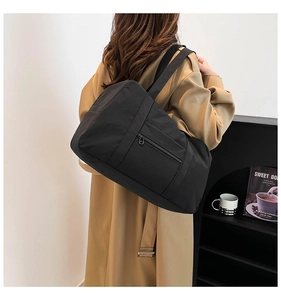 Detail of black nylon tote bag featuring wide shoulder straps and side zipper pocket