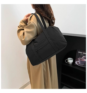 Detail of black nylon travel tote featuring a convenient front zipper pocket and light texture