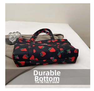 Detail shot of the durable reinforced base of a black tote bag with red strawberry print