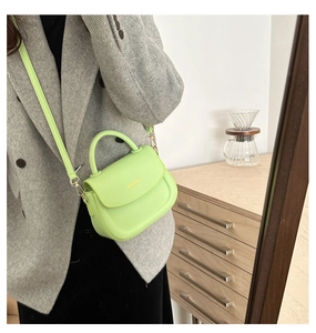Detail of neon green leather crossbody bag featuring gold lettering and metal hardware