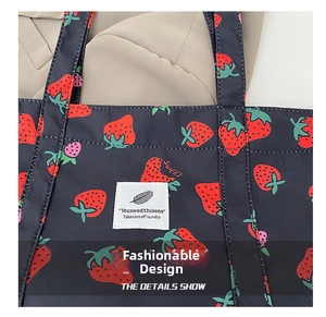 Detail of black nylon tote bag featuring red strawberry print and white woven brand label