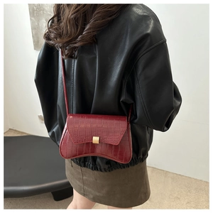 Detail of burgundy crocodile pattern baguette bag with gold buckle on a model shoulder