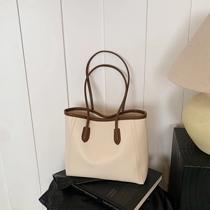 Minimalist beige tote bag with brown handles on a leather garment in a cozy room