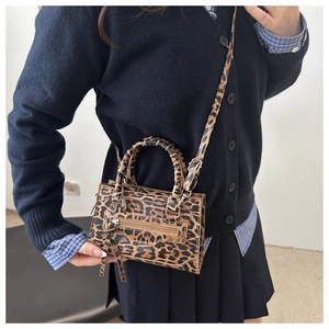 Dettaglio di piccola borsa quadrata leopardata con manici tondi e nappine decorative