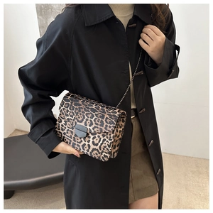 Detailed close-up of leopard print crossbody bag with matte black shield buckle and metal chain