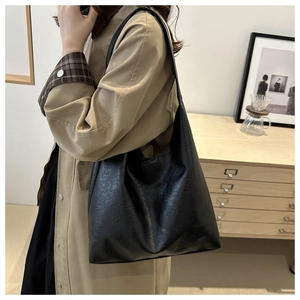 Side view of large black leather tote bag worn with a khaki trench coat for commute