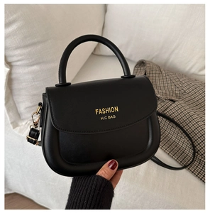 Close-up of black fashion saddle bag with gold lettering held against a soft background
