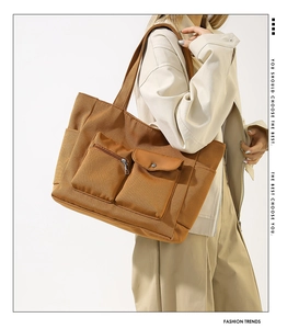 Detail of caramel tote bag showing a metal zipper pocket and a functional flap button pocket