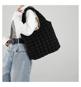 Detailed texture of black quilted bubble tote bag shown on model with shoulder strap