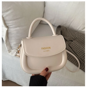 Close-up of a cream saddle handbag featuring a gold logo and soft faux leather texture