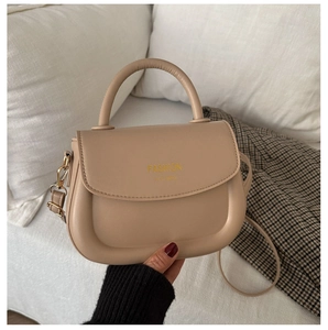 Detail of beige faux leather saddle bag with gold hardware and embossed fashion logo