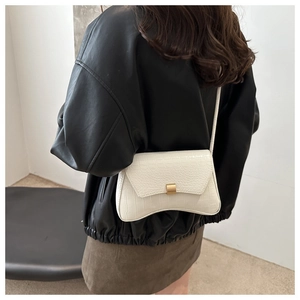 Detail of white croc-embossed underarm bag with gold clasp on black leather jacket