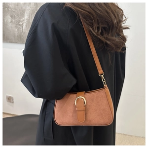 Brown suede underarm bag with vintage buckle shown worn by a model in a minimalist setting