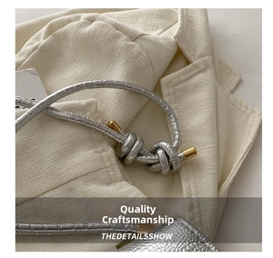 Close-up of silver textured knot shoulder strap with gold metallic tips on the bag