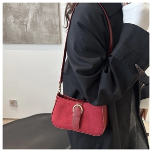 Detail of red suede shoulder bag with gold metal buckle shown on a black coat