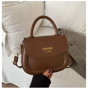 Detail of dark brown saddle handbag with round handle and gold brand lettering