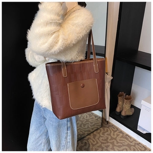 Detail of vintage brown leather tote bag with woven texture worn with white plush coat