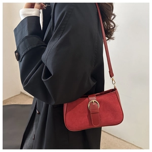 Detail of red suede underarm bag with vintage buckle worn with a black coat