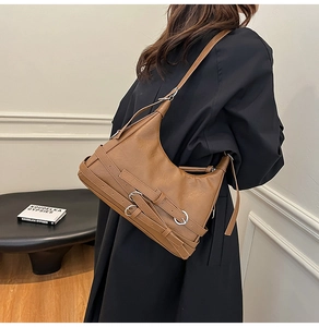 Detail of a brown leather tote bag with silver buckles and vintage motorcycle style straps