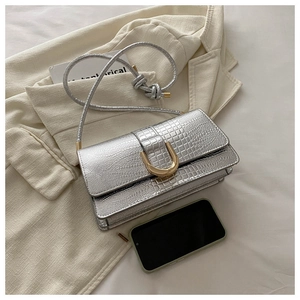 Detail of silver crocodile-patterned crossbody bag with a gold U-shaped metal buckle
