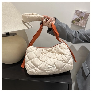 Detailed view of beige quilted puffer bag with vibrant orange strap and fashion label