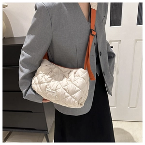 Detail of beige quilted puffer bag with orange strap and fashion label on front