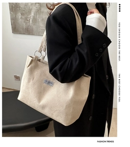Detail of beige corduroy tote bag featuring metal ring hardware and small logo patch