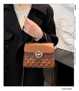 Detail of caramel leather handbag featuring a metal clover twist lock and quilted texture