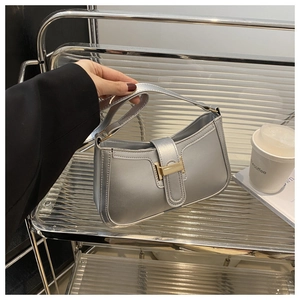 Detailed shot of a silver metallic shoulder bag with golden H-shaped clasp and leather strap