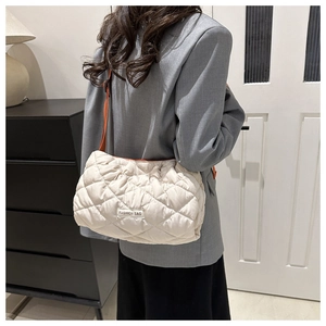 Detail of beige quilted puffer bag with rhombus pattern and brown shoulder strap on model