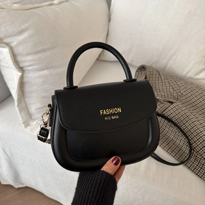Minimalist black matte leather saddle bag with gold lettering and top handle on sofa