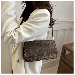 Detail of leopard print shoulder bag with gold hardware worn over a white coat