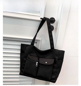 Detail of black nylon tote bag with functional exterior pockets and zipper closures