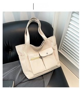 Detail of off-white nylon tote bag with zipper and buckle pockets on a black leather chair