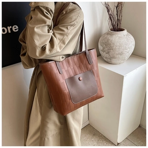 Detail of woven brown leather tote bag with a suede pocket and decorative round buckle