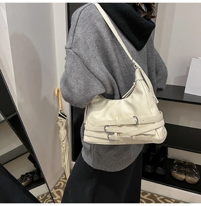 Detail of cream motorcycle crossbody bag with silver buckle straps worn by a model
