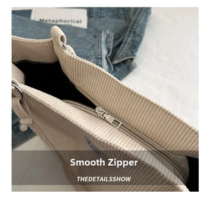 Detail shot of a beige corduroy tote bag showing silver metal zipper and soft fabric texture