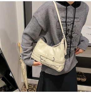 Detail of cream-colored crescent bag with textured pleats and silver buckle straps