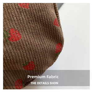 Close-up of brown corduroy fabric with red strawberry embroidery on a casual bag