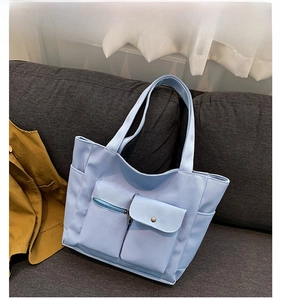 Detail of light blue canvas tote bag showing front zipper pocket and button flap design