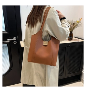 Detailed view of brown leather tote bag with gold buckle on a model in a warm setting
