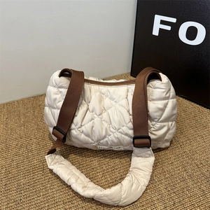Cream quilted puffer tote bag with brown straps on a woven mat for winter fashion