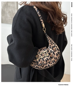 Detailed view of leopard print crescent bag with gold buckle on a black coat