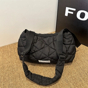 Black quilted puffer tote bag with diamond pattern and crossbody strap on woven mat