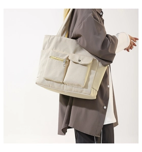 Detail of beige nylon tote bag featuring front zipper and snap button utility pockets
