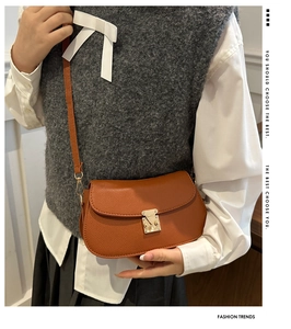 Detail of caramel brown saddle bag featuring lychee texture and gold metal buckle lock