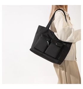 Detail of black nylon tote bag showing external zipper pocket and metal snap button flap pocket