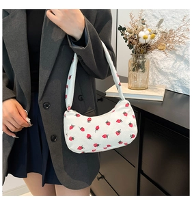Close-up of white corduroy shoulder bag with strawberry print held by a model