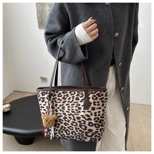Détail d'un sac cabas léopard avec poignées en cuir marron et pendentif ours peluche