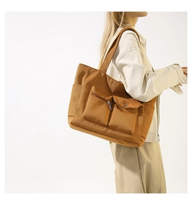 Detail of nylon tote bag featuring front zipper pocket and button flap compartment